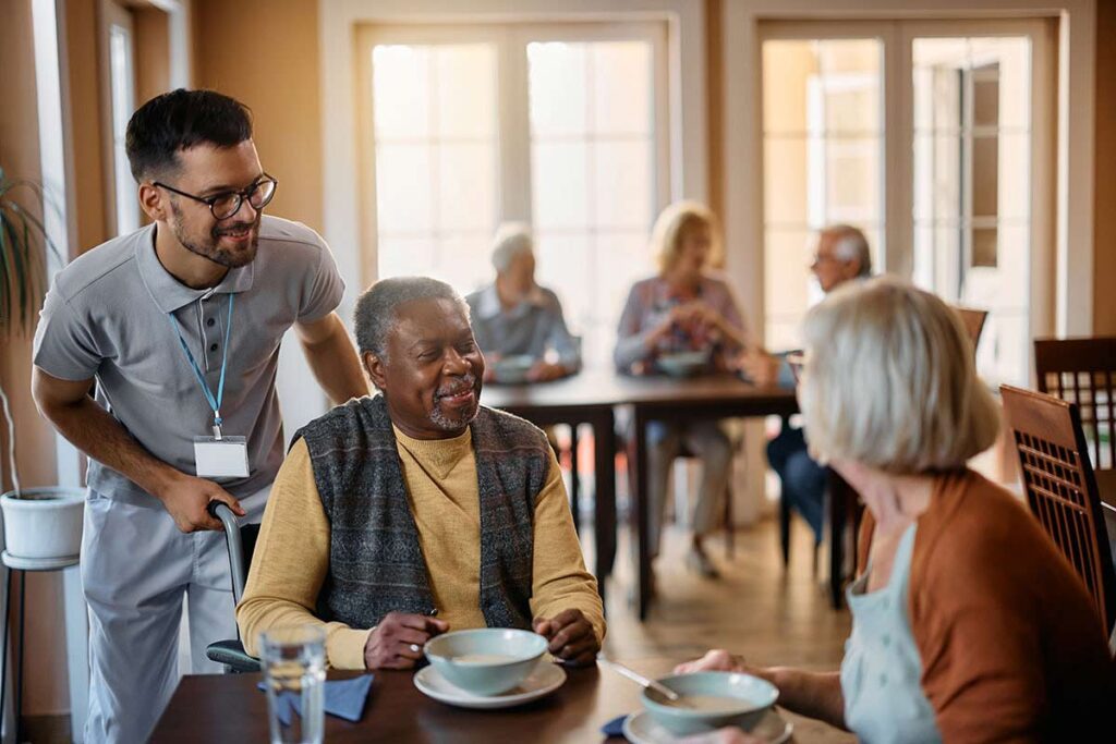 The Avenues of Fort Bend | Young healthcare worker and senior people during lunch at nursing home.